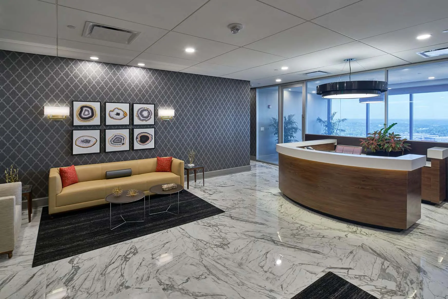 Modern office lobby with marble floors, a curved wooden reception desk, a yellow sofa, and framed artwork on a patterned wall. Large windows provide a city view and showcase the impressive Simmons Tower amenities.