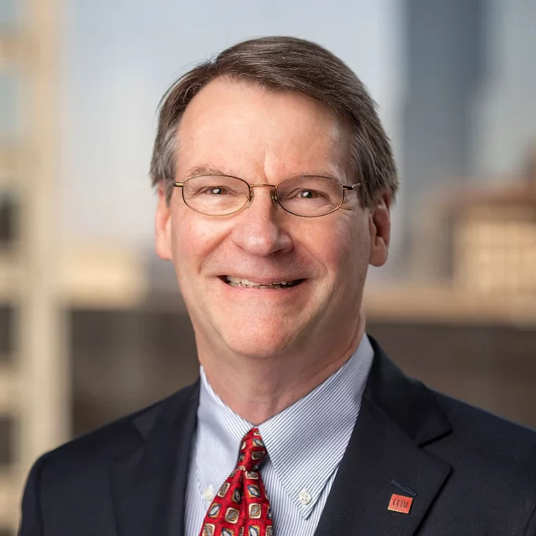 Bill Puddephat, a smiling man with glasses, short brown hair, and a suit with a red patterned tie.