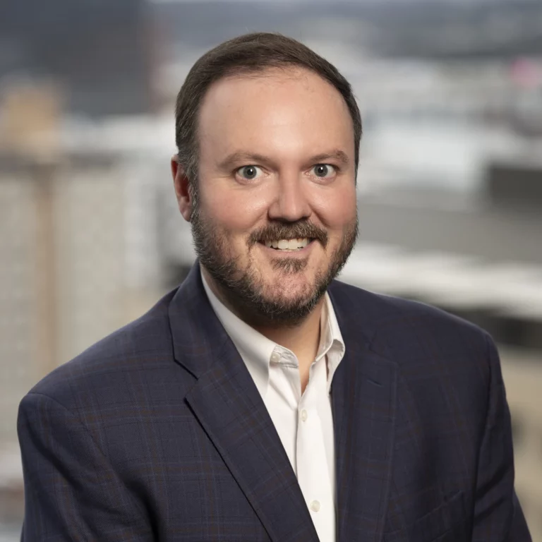 Brandon Sheard, a man with short brown hair and a beard, is seen smiling while wearing a dark blue plaid suit jacket.